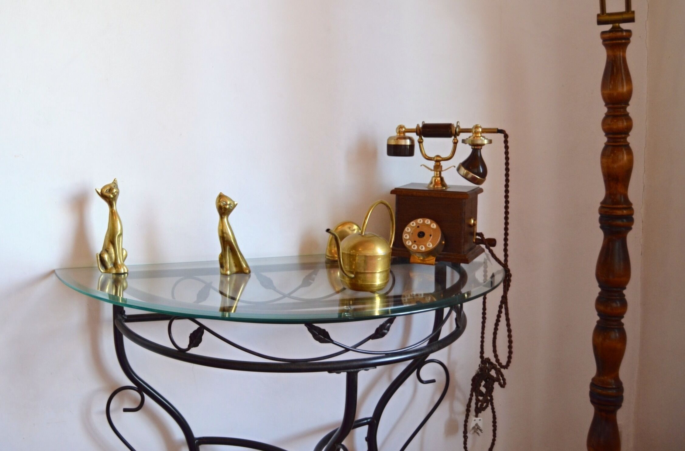 Une table dont le plateau est en verre, agrémentée d’un téléphone ancien, de statuettes en laiton et d’une théière.