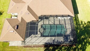 An aerial view of a modern building with a large glass-enclosed swimming pool, multiple roof sections, and surrounding green lawns. - Spacious & Private Guest Pool House Oasis (Orlando)