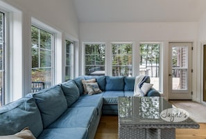 A modern living room with a blue sectional sofa, large windows, and a glass coffee table.