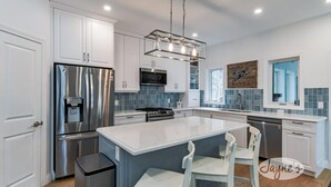 Een moderne keuken met witte kasten, een roestvrijstalen koelkast, een inbouwfornuis en een groot eiland met twee witte stoelen.