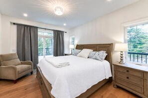 A bedroom with a bed, a chair, a nightstand, and a window with a view of greenery.