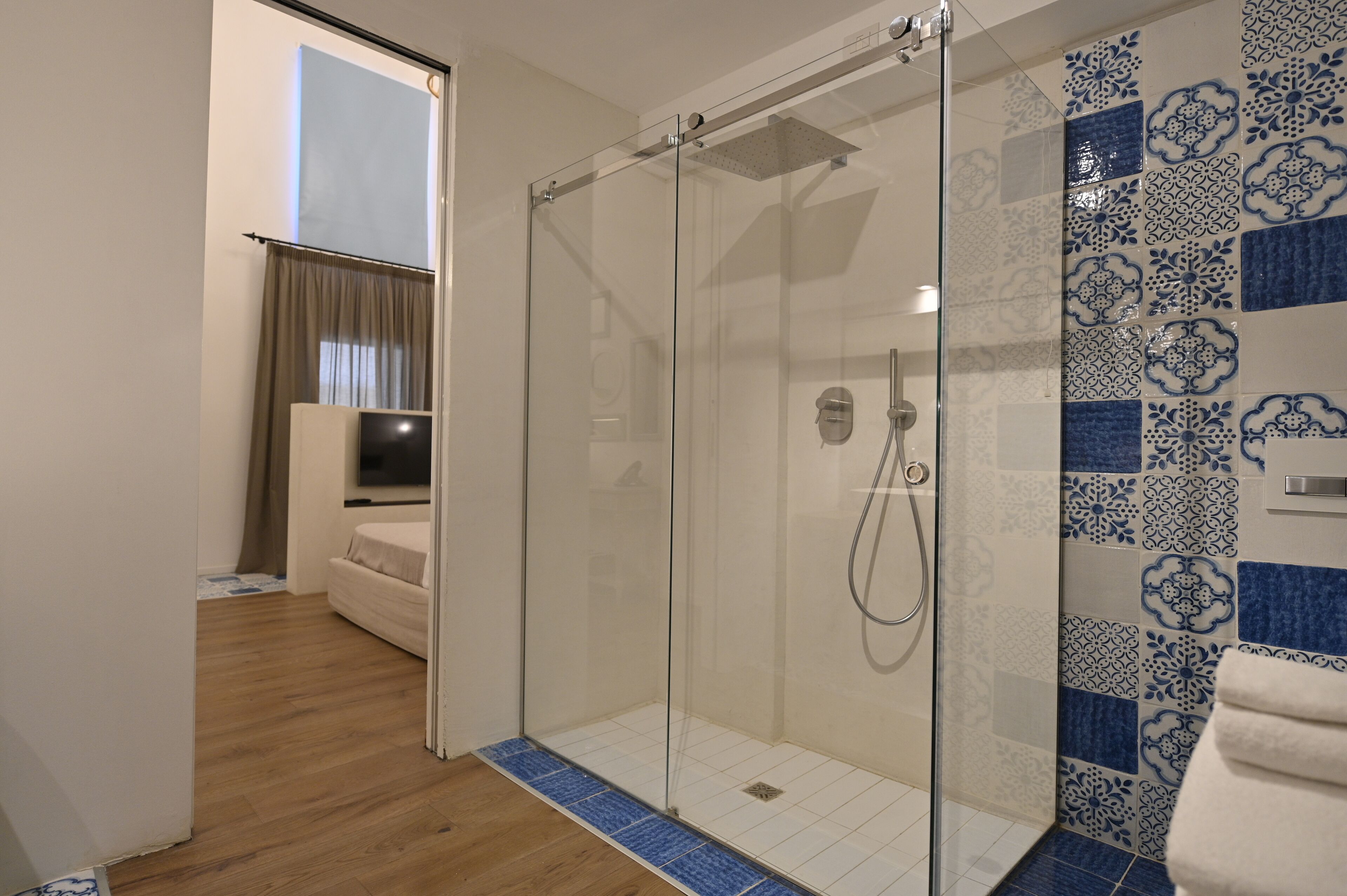 A modern bathroom with a glass-enclosed shower, a wooden floor, and patterned tiles.