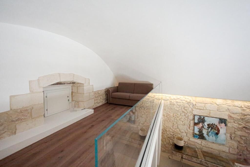 A loft-style room with a stone wall, a glass railing, a fireplace, and a brown sofa.