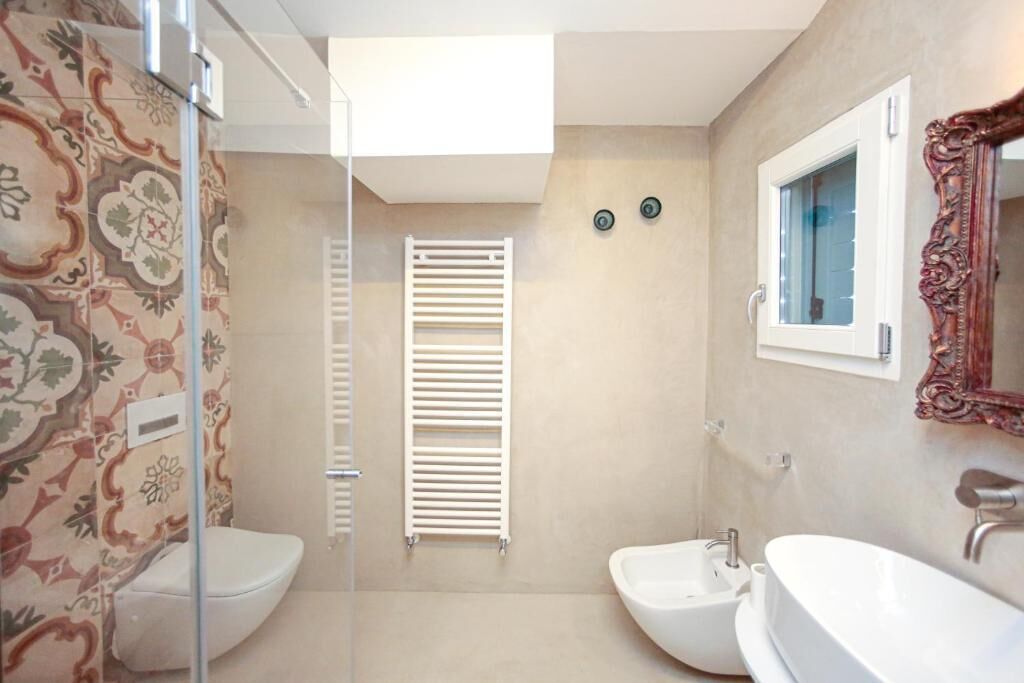A bathroom with a toilet, bidet, and sink, a mirror, and a window.