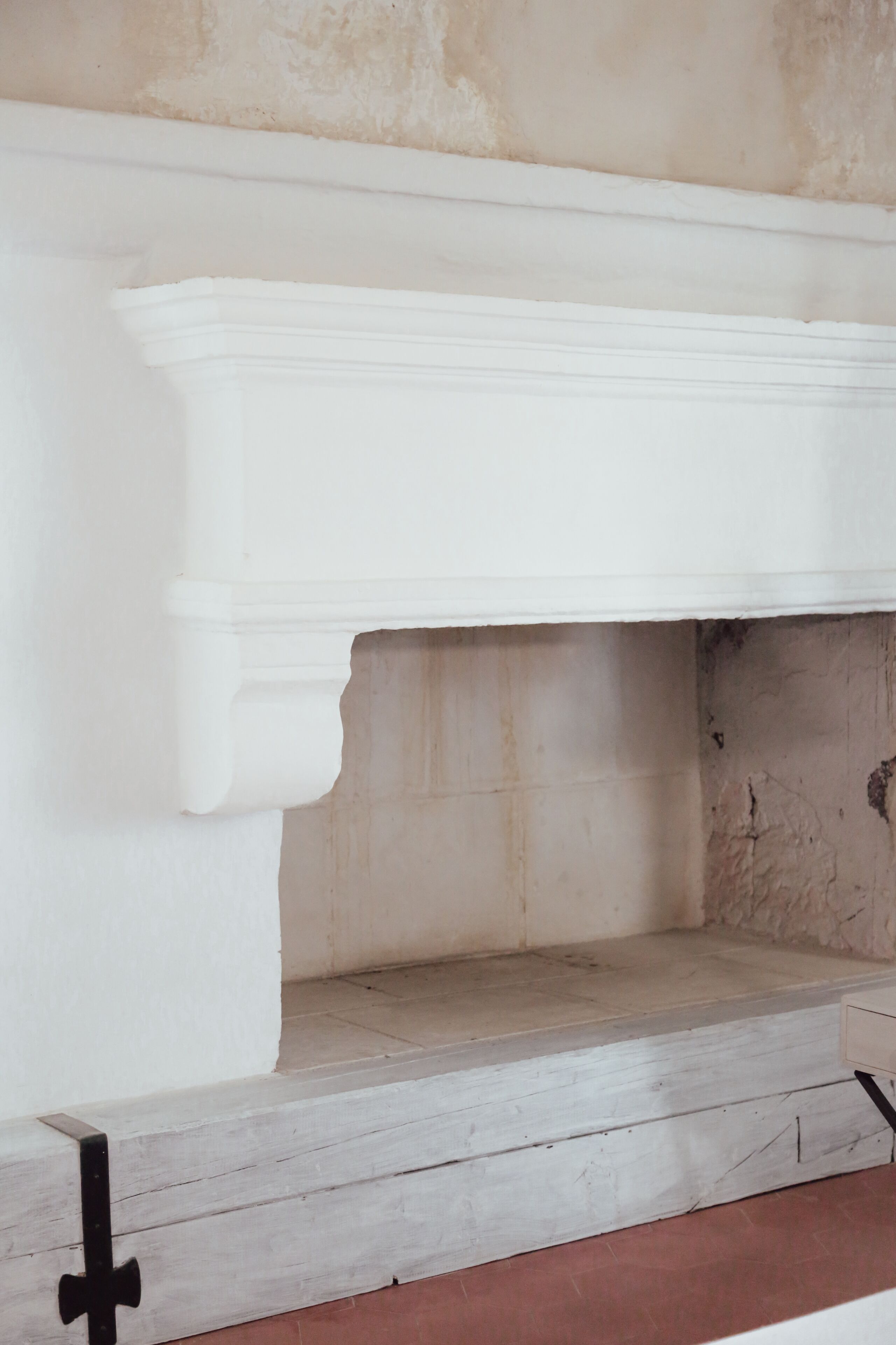 Una chimenea blanca con base de piedra, ubicada en una habitación con pared lisa y suelo rojo.