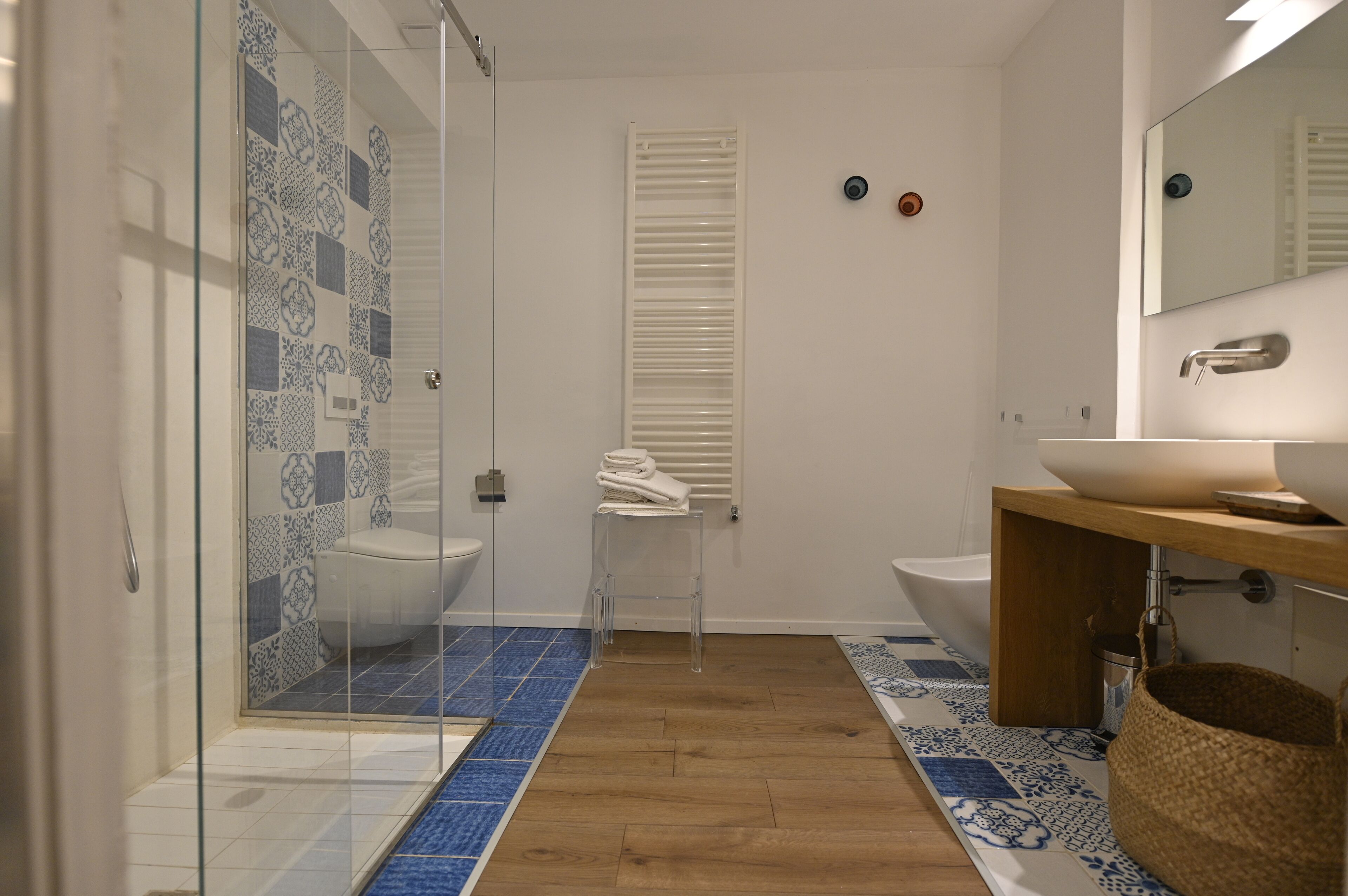 Un baño moderno con cabina de ducha de vidrio, dos lavabos, un mueble de tocador de madera y azulejos estampados.