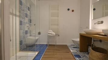 Un baño moderno con cabina de ducha de vidrio, dos lavabos, un mueble de tocador de madera y azulejos estampados.