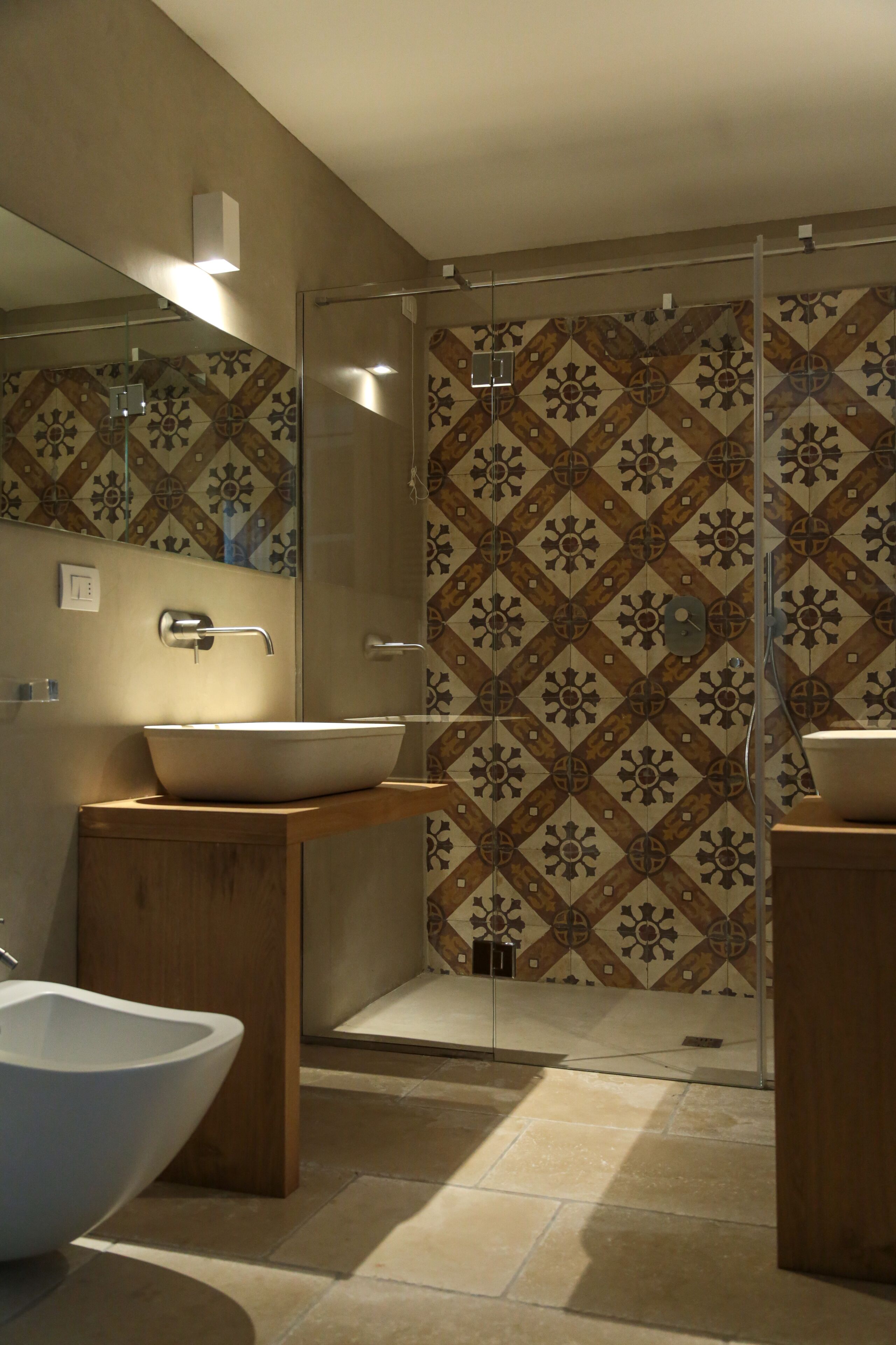 A modern bathroom with a large vessel sink, a glass-enclosed shower, and patterned tile walls.
