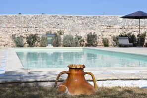 Un muro de piedra, una piscina y un florero sobre el césped.