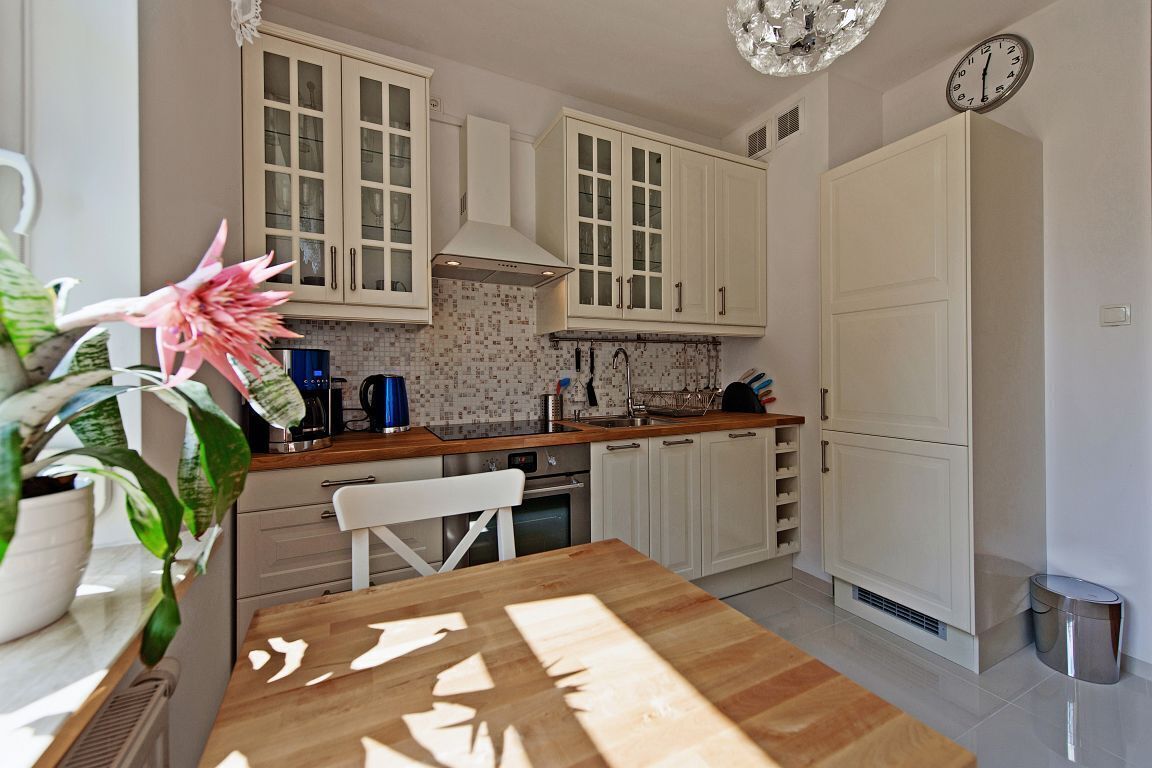A modern kitchen with white cabinetry, a wooden table, and a potted plant.