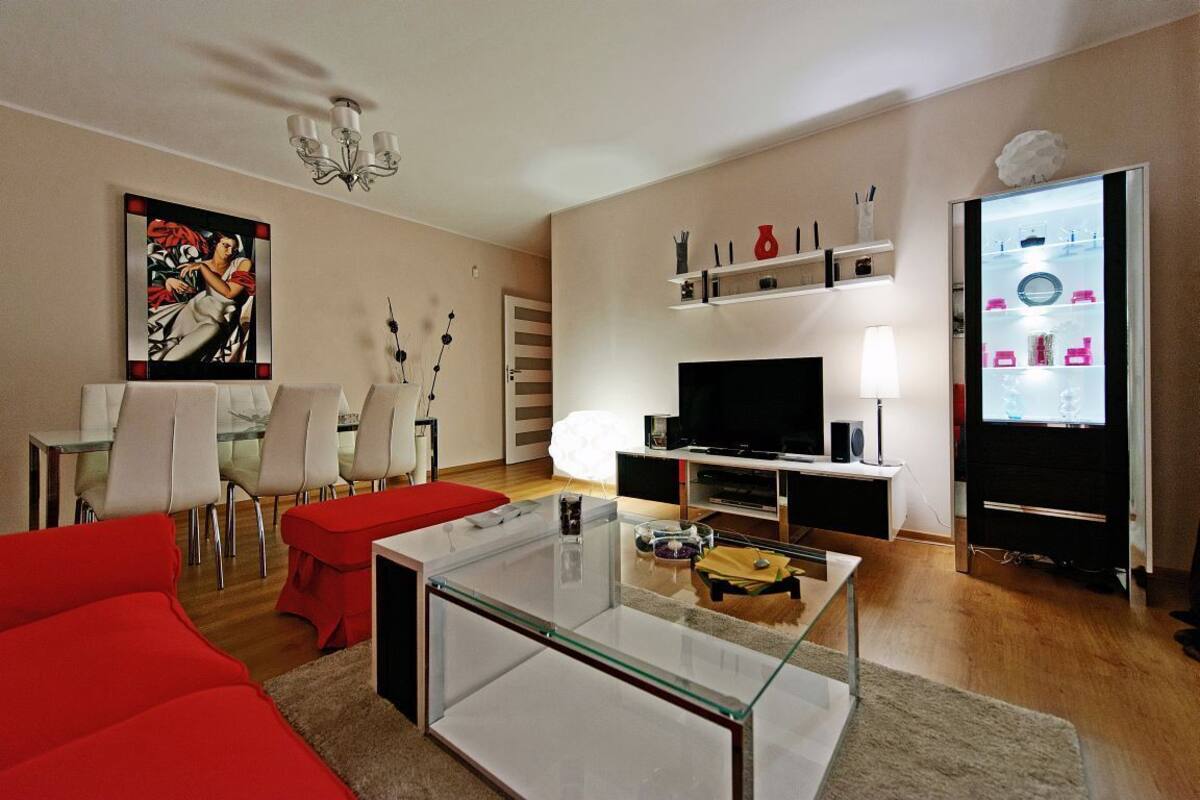 A modern living room with a glass coffee table, red sofa, and a flat-screen TV.