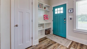 A hallway with a white door, a teal door, and a shelf with decorative items. - Bright beach house steps from the sand & memories (Long Beach)
