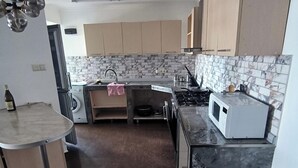 A compact kitchen with a washing machine, a microwave, and a stove. - House by the sea Kaprovani Shekvetili Batumi (Ureki)