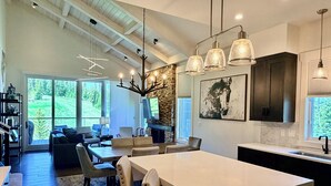 A spacious living area with a large dining table, comfortable seating, a fireplace, and a stone accent wall. - Ski-in/out from Back Door, Mtn Modern Moonlight Basin "Wildwood Luxury Chalet", Hot Tub, Garage (Big Sky)