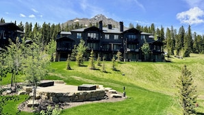 A large, multi-story lodge with a stone patio and a mountain backdrop. - Ski-in/out from Back Door, Mtn Modern Moonlight Basin "Wildwood Luxury Chalet", Hot Tub, Garage (Big Sky)