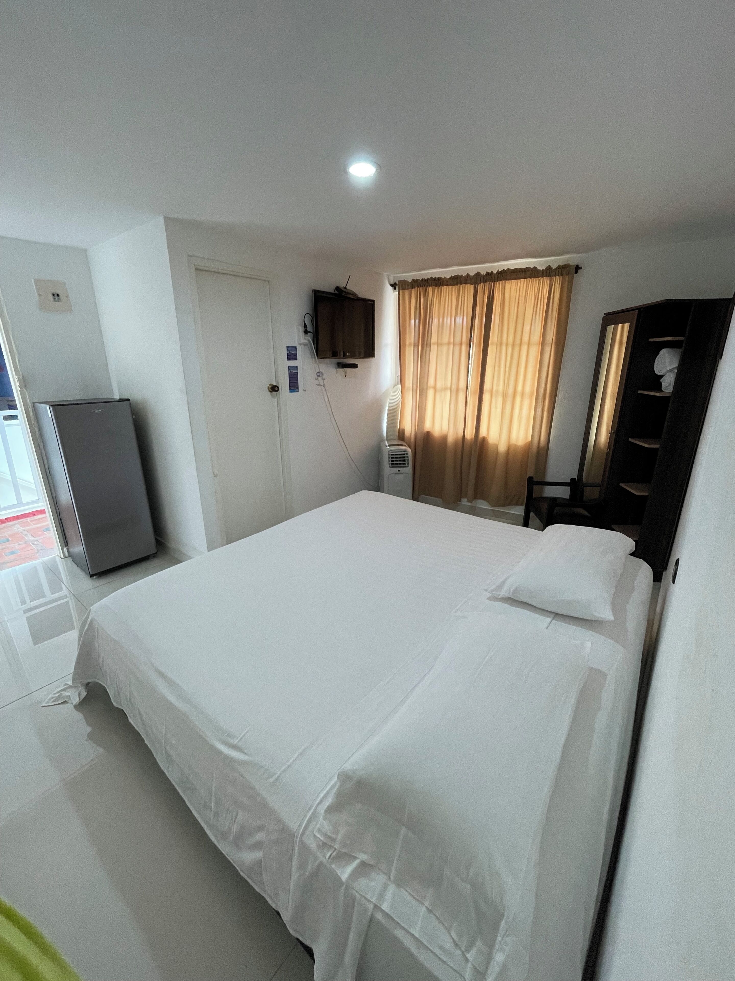 Une chambre d’hôtel avec un lit, un téléviseur fixé au mur, un radiateur, une armoire et une porte.