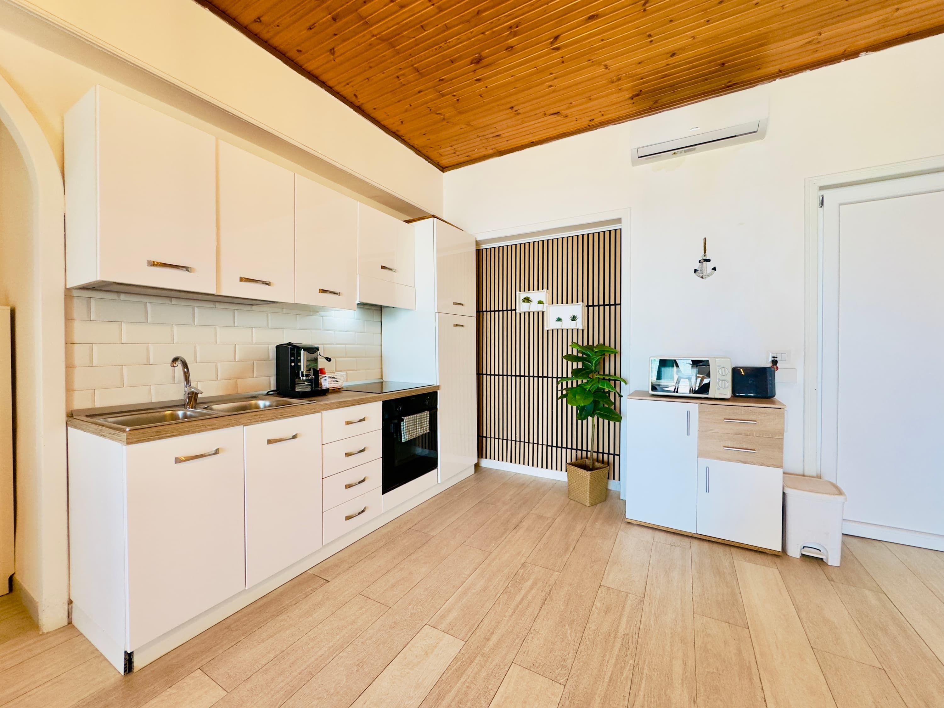 A modern kitchen with white cabinets, a wooden ceiling, and a built-in oven.
