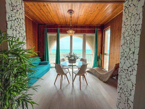 A dining area with a table and chairs, a hanging light fixture, a view of the ocean, and a stone wall. - Athena Seafront Apartment, Parking & Pool (Castel Volturno)