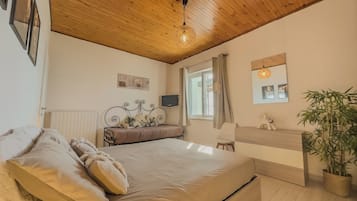 A bedroom with a wooden ceiling, a bed with pillows, a bedside table, a mirror, a window with curtains, and a potted plant.