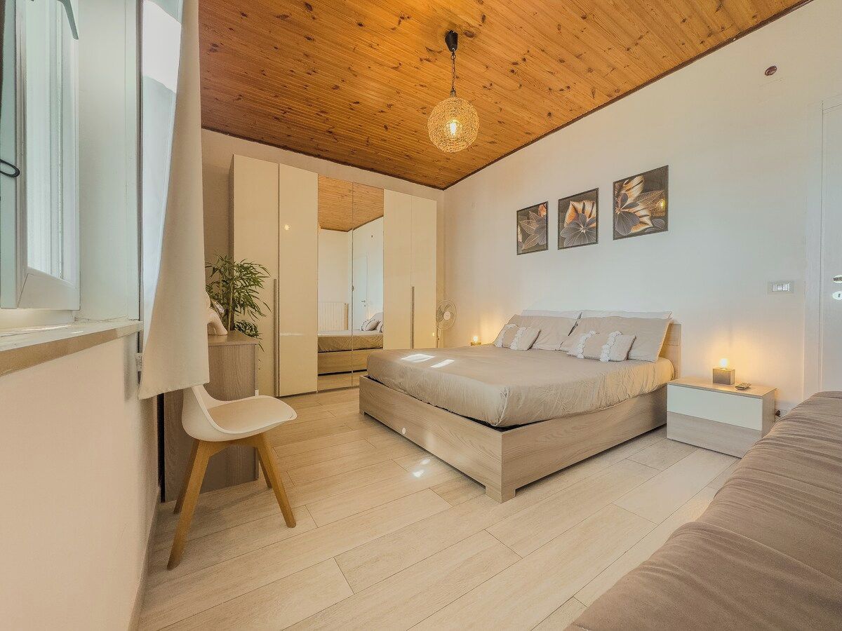 Une chambre à coucher avec un lit, des tables de chevet, une chaise, une plante et des œuvres d’art accrochées au mur.