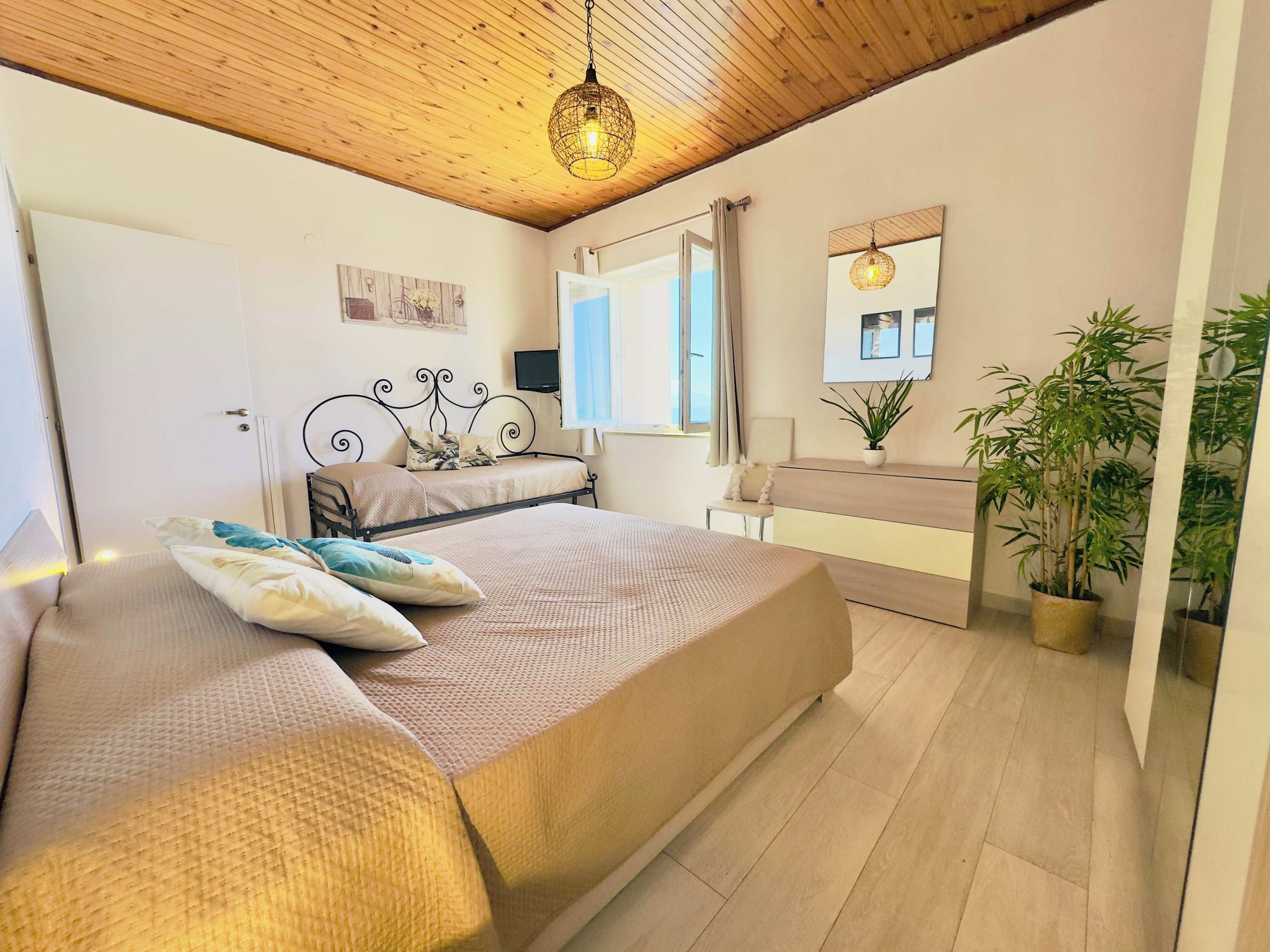 Ein Schlafzimmer mit einem Bett, Nachttisch, Topfpflanzen und einem Fenster.