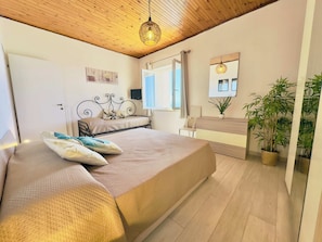 A bedroom with a bed, bedside table, potted plants, and a window. - Athena Seafront Apartment, Parking & Pool (Castel Volturno)