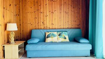 Ein Zimmer mit einem blauen Sofa, einer Holzwand, einer Lampe und einem Vorhang.