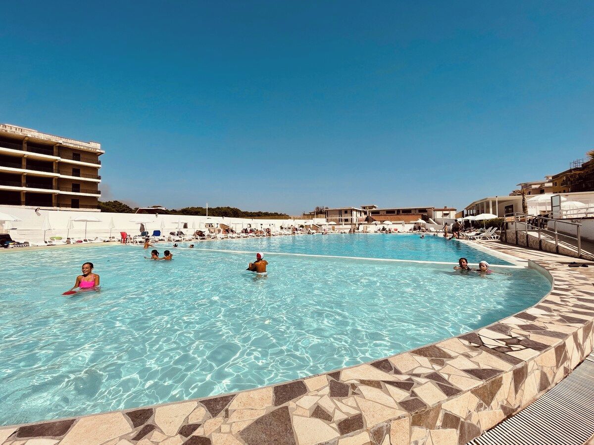 A large outdoor swimming pool with clear blue water, surrounded by lounge chairs and umbrellas.