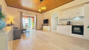 A modern living space with a wooden ceiling, a kitchen with white cabinets, a dining area with a table and chairs, and a TV mounted on the wall.