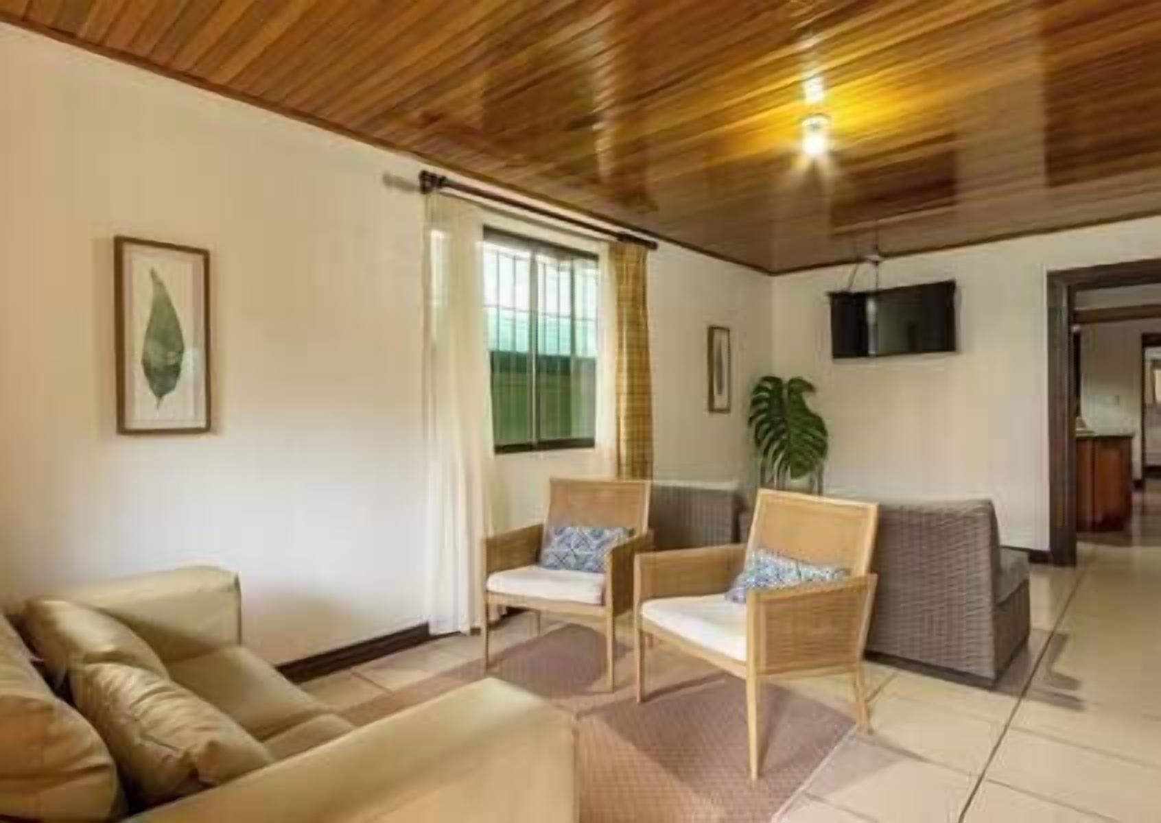 Una sala de estar con techo de madera, un sofá, dos sillones, un televisor y una planta.
