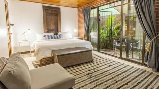A bedroom with a bed, a sofa, a small table, and a sliding glass door leading to an outdoor area. - Tikita family house in La Fortuna downtown (La Fortuna)