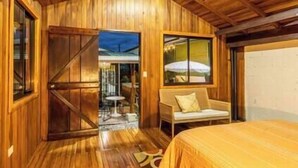 A wooden room with a bed, a window with an umbrella, and a door leading to an outdoor area. - Tikita family house in La Fortuna downtown (La Fortuna)