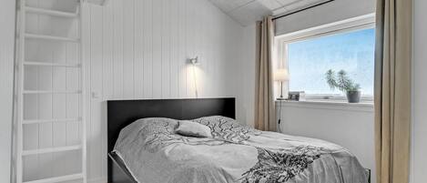 A bedroom with a bed, a nightstand, a lamp, a window with curtains, and a view of the outdoors.