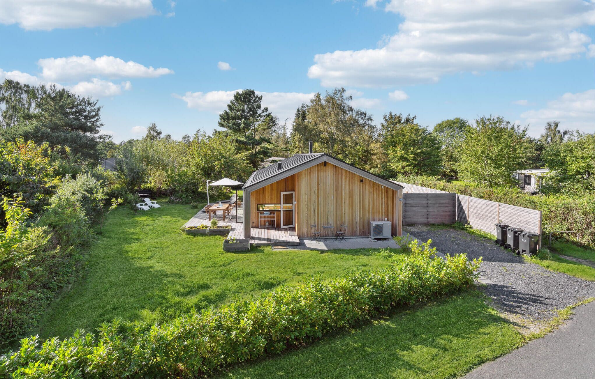 Una cabaña de madera con terraza, rodeada de abundante vegetación y árboles.