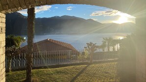 Blick durch eine Bogenkonstruktion aus Stein auf ein Gewässer mit Bergen im Hintergrund.
