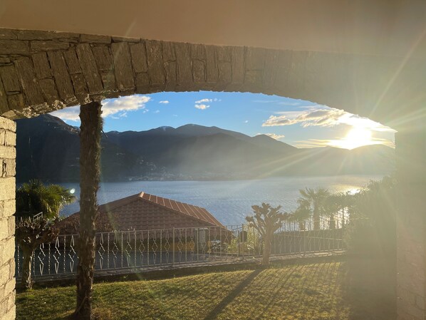 A view through an arched stone structure overlooking a body of water with mountains in the background.