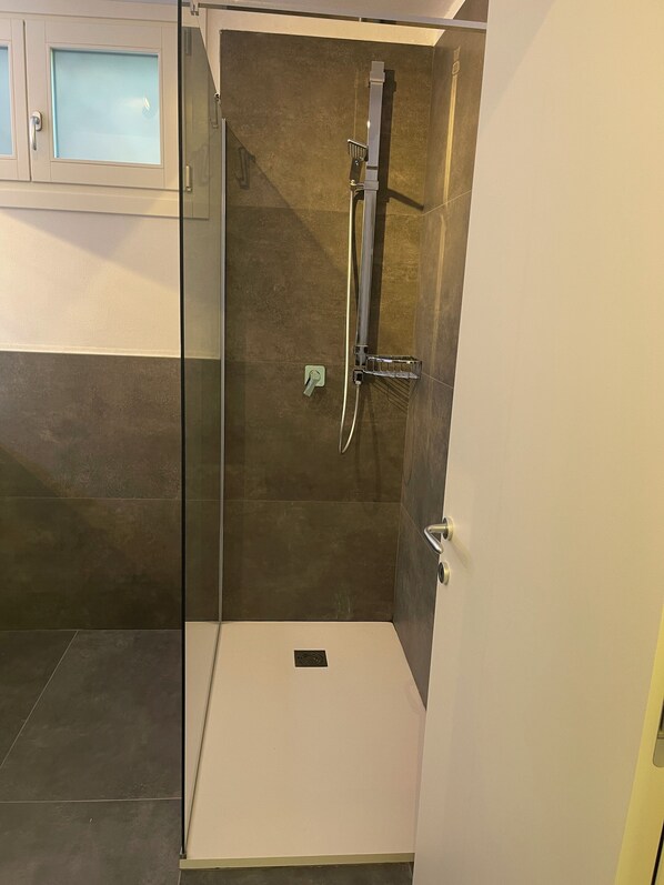 A modern bathroom with a glass-enclosed shower, a white sink, and a tiled floor.