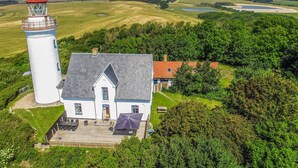 Ein Leuchtturm und ein Haus mit befestigter Auffahrt und einer Sitzgelegenheit im Freien.