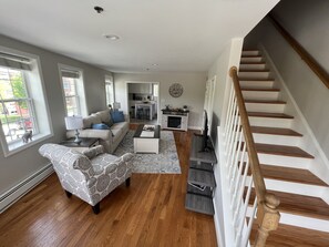 A spacious living room with a sofa, armchair, coffee table, and a staircase.