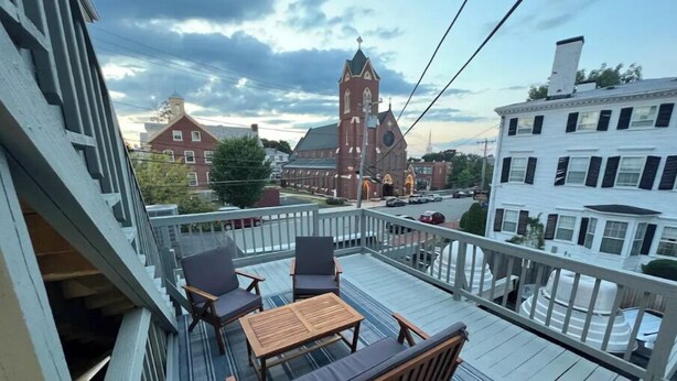 Un balcone con mobili in legno e vista su un edificio storico con una torre dell'orologio.