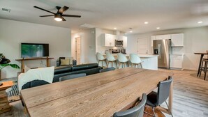 A modern living room with a wooden dining table, a sofa, and a TV. - The Starlight Retreat | Clean. Bright. Modern. (Redding)