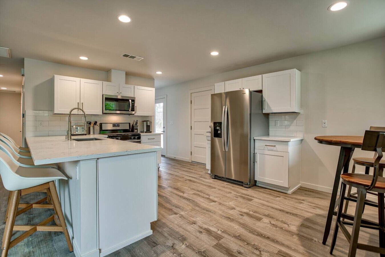 A modern kitchen with white cabinetry, stainless steel appliances, and a wooden floor.