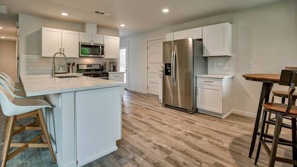 A modern kitchen with white cabinetry, stainless steel appliances, and a wooden floor. - The Starlight Retreat | Clean. Bright. Modern. (Redding)