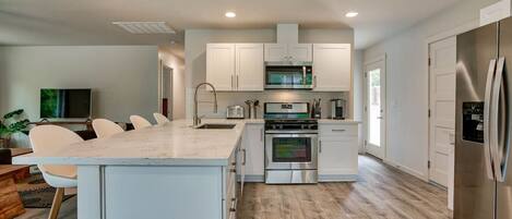 A modern kitchen with white cabinetry, a central island, stainless steel appliances, and a dining area with chairs.