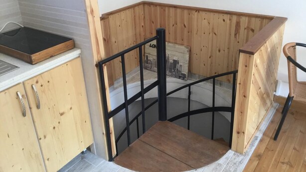 A corner of a room with wooden paneling, a black metal staircase, and a small table with a black surface. - Charming 1-bed Apartment in Larnaca (Larnaca)