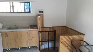 A compact kitchen with a sink, wooden cabinets, a small window, and a dining area with a chair. - Charming 1-bed Apartment in Larnaca (Larnaca)