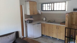 A compact kitchen with wooden cabinets, a white refrigerator, a sink, and a window above the counter. - Charming 1-bed Apartment in Larnaca (Larnaca)