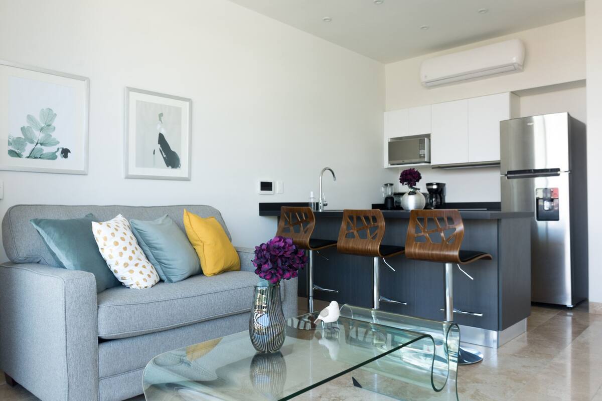 Eine moderne Küche mit einem grauen Sofa, einem Glastisch und einer Vase mit Blumen.