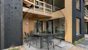Un bâtiment moderne à deux étages, doté d’un balcon, d’un coin repas avec une table et des chaises, et de grandes fenêtres.