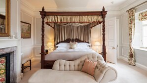 A four-poster canopy bed with a tufted headboard, a fireplace, and a sofa with a decorative pillow. - Cornish Castle - Luxury Cottages (Saltash)